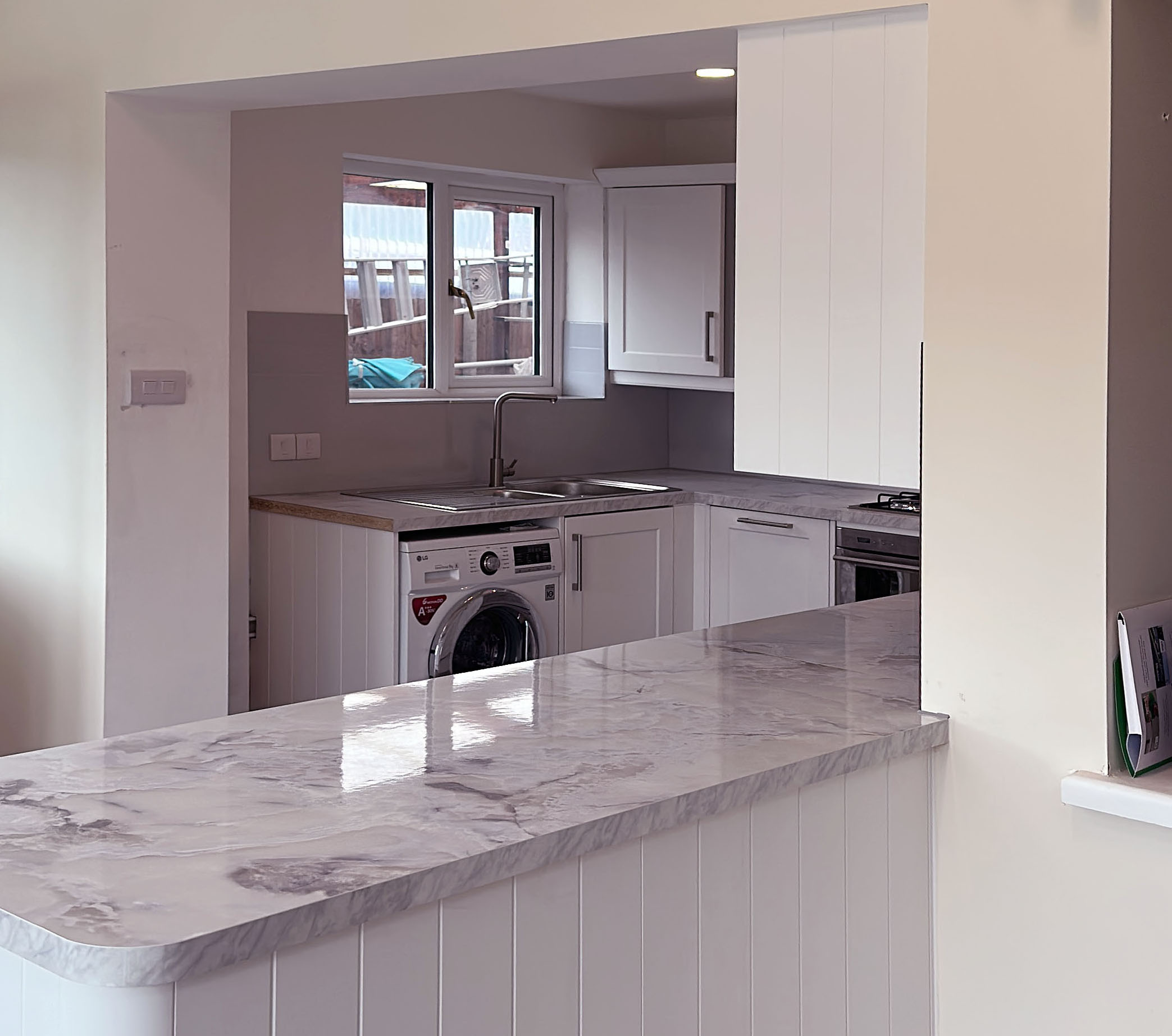 A finished kitchen with marble worktops and a breakfast bar by L&P Developments